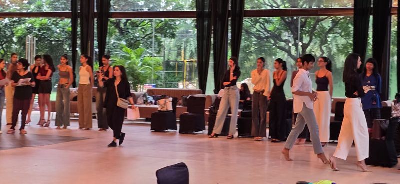 Models walking in a line during a rehearsal inside a glass-walled event pavilion
